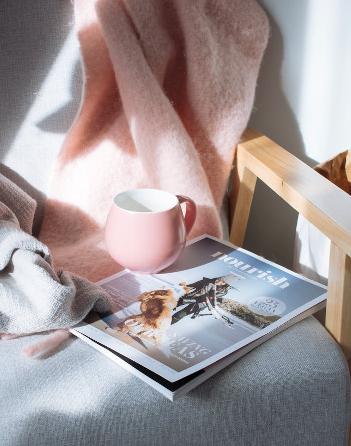 services-02 A warm scene featuring a pink mug and magazine on a wooden chair, bathed in sunlight.