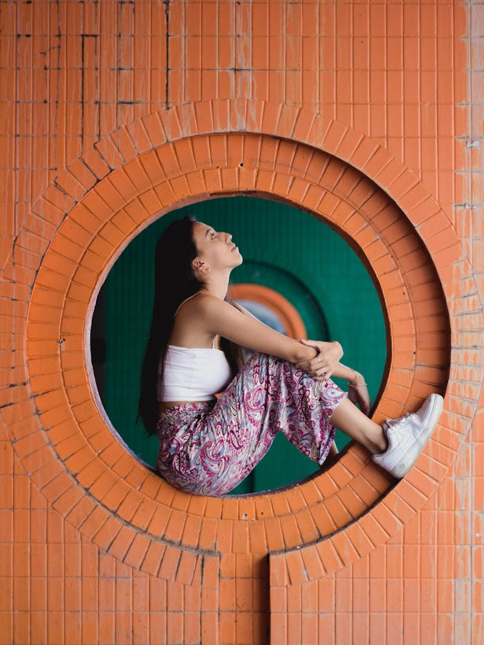 services-03 Young woman sitting in round brick opening, embracing a moment of reflection in George Town.